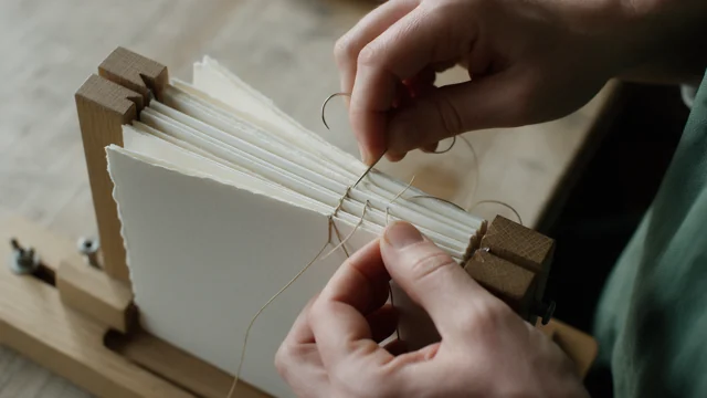 An artisan sewing the pages of a book by hand with linen thread.